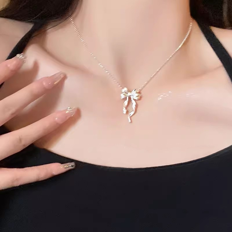 Model wearing a silver ribbon bow pendant necklace with a black top, showing the elegant pendant and necklace fit