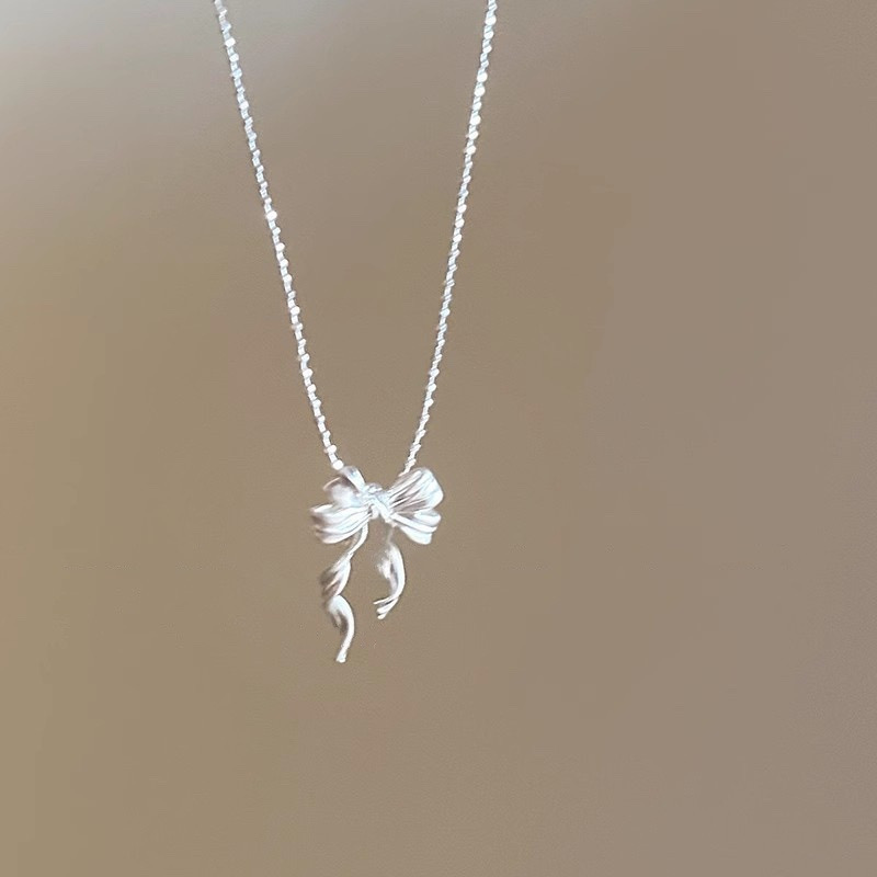 Front view of silver ribbon bow pendant necklace featuring a dimensional bow and two flowing ribbon tails