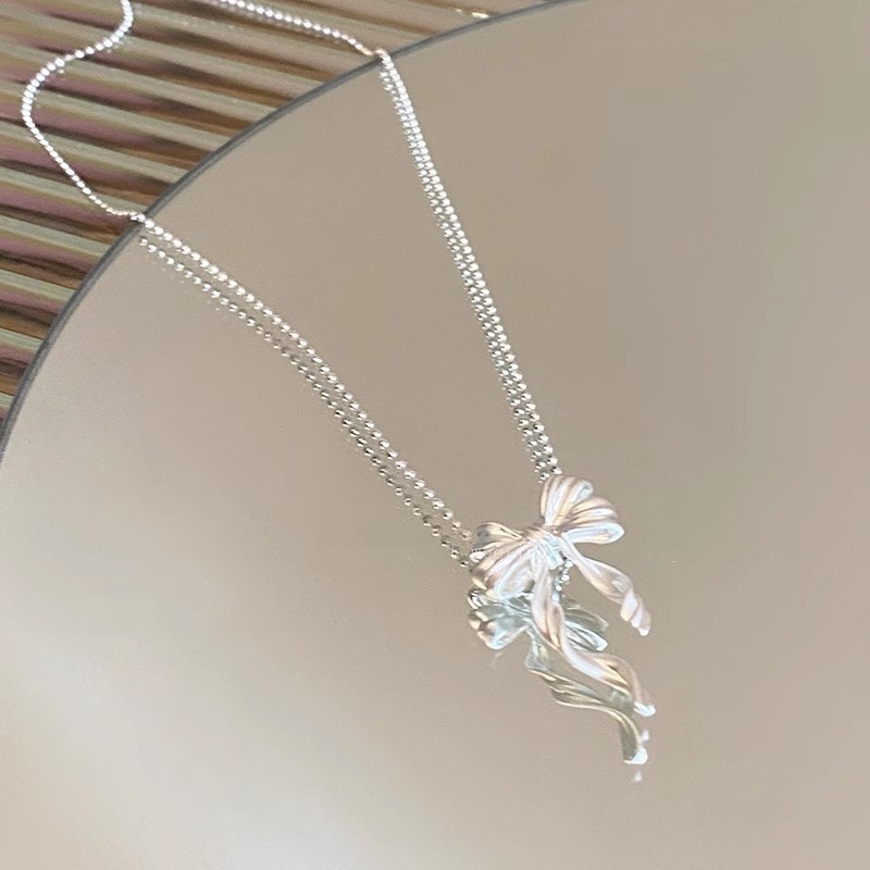 Detailed view of silver ribbon bow necklace pendant with sculpted loops and softly curved dangling ribbon tails