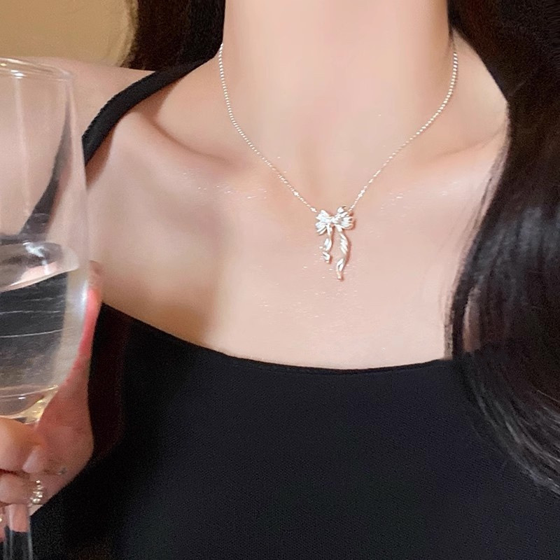 Model wearing a silver ribbon bow pendant necklace with a black outfit while holding a glass