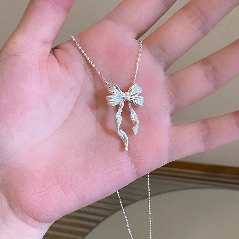Close-up of silver ribbon bow pendant necklace held in hand, highlighting the sculpted bow and flowing ribbon tails