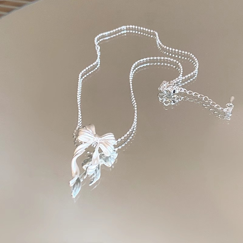 Silver ribbon bow pendant necklace laid flat, showing the delicate beaded chain, bow pendant and adjustable extension chain