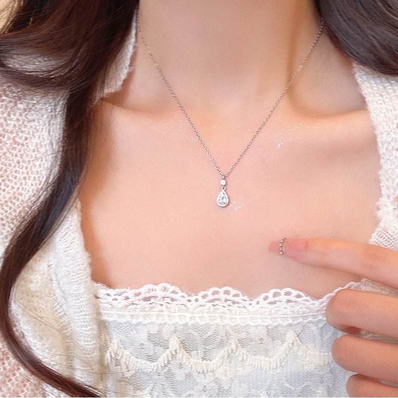 Woman wearing a delicate silver zircon teardrop pendant necklace with a white lace outfit
