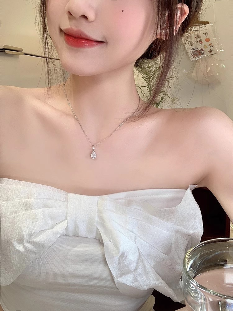 Woman wearing a silver zircon teardrop pendant necklace with a white bow-detail top