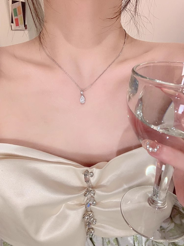 Close-up of silver zircon teardrop pendant necklace worn with an elegant white satin dress