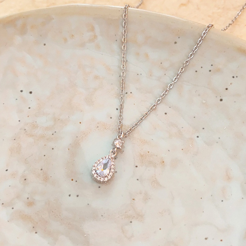 Silver zircon teardrop pendant necklace with sparkling stone accents displayed on a ceramic plate