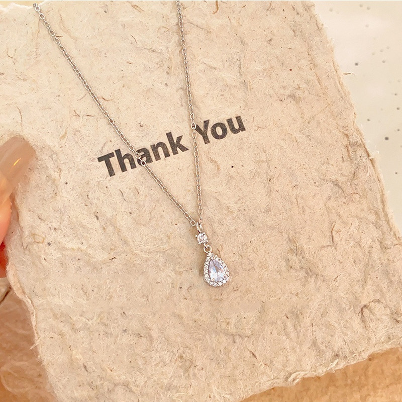 Silver-tone teardrop zircon pendant necklace displayed on textured paper showing the chain and pendant design