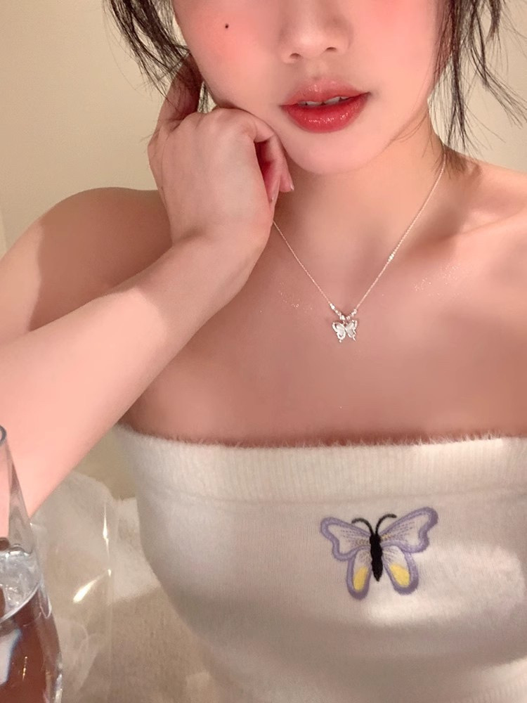 Model wearing a silver butterfly pendant necklace with a white butterfly embroidered top for a feminine look