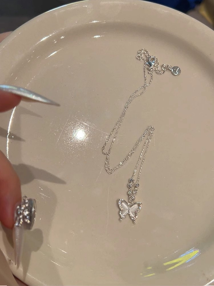 Silver cat eye butterfly pendant necklace laid on a white plate showing the delicate chain, butterfly pendant and clasp