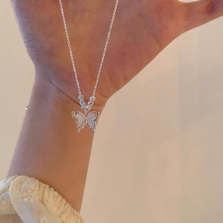 Silver butterfly pendant necklace with white cat eye stone and rhinestone accents displayed against a wrist