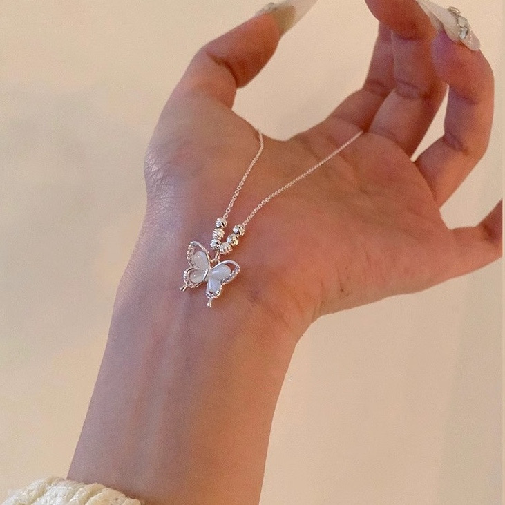 Close-up of silver cat eye butterfly pendant necklace with delicate chain and sparkling rhinestone details held over a hand