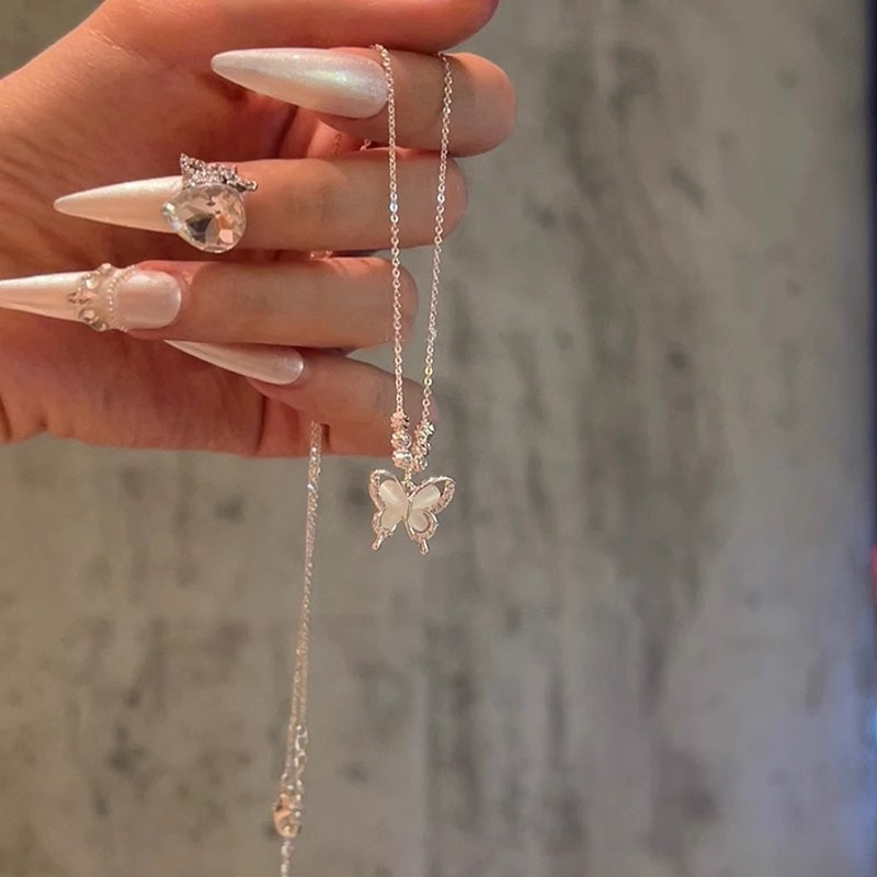 Silver butterfly pendant necklace held by hand, showing the delicate chain, white cat eye stone and butterfly design