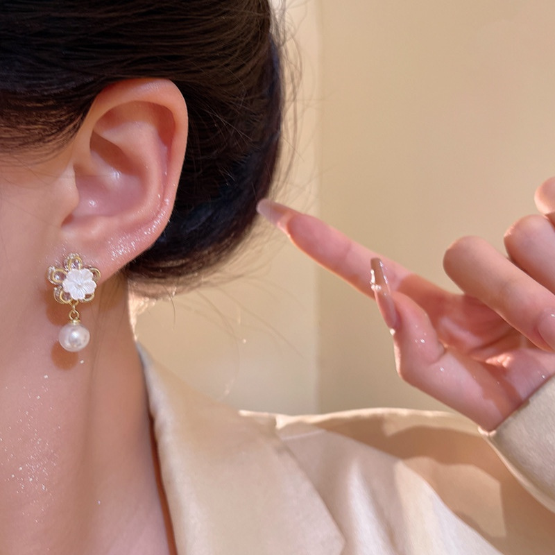 Gold floral pearl drop earrings on ear