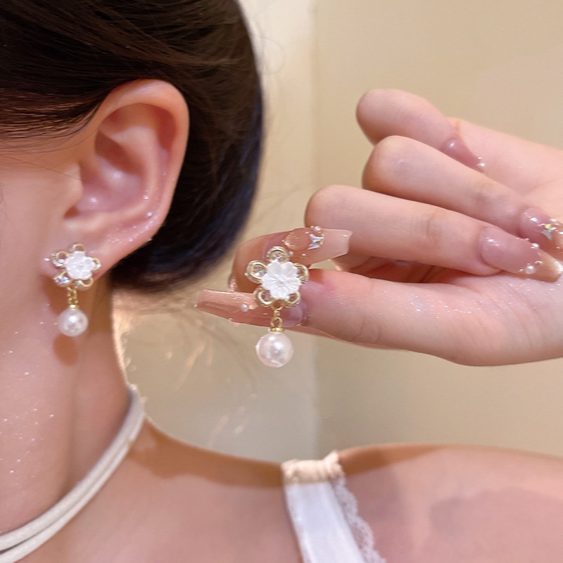 Gold flower pearl drop earrings worn on ear