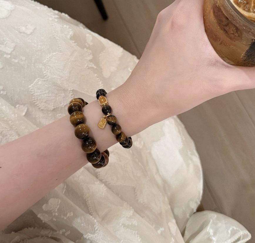 Elegant wrist wearing Tiger’s Eye bracelets holding a glass of iced drink