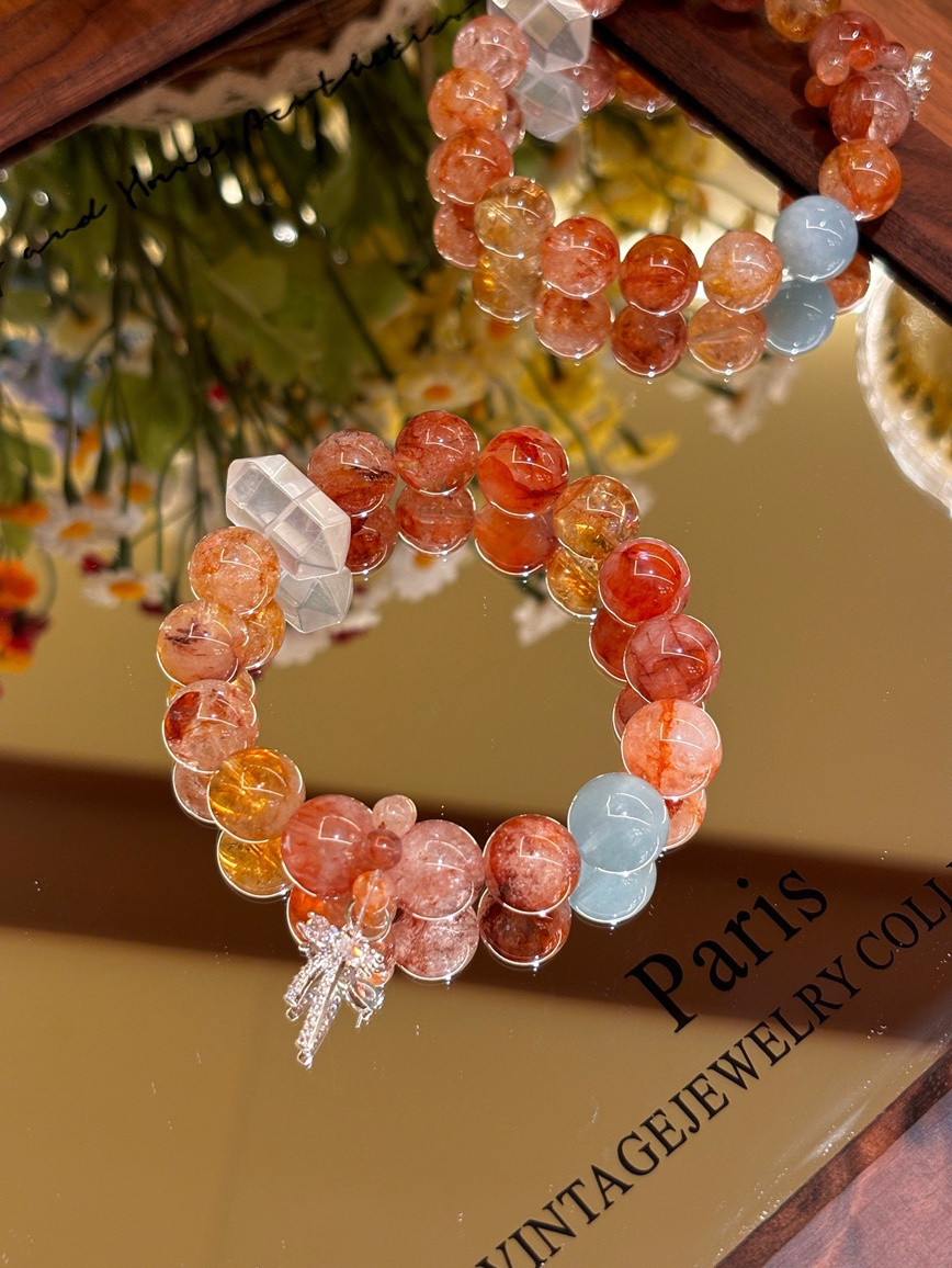 Red flower and aquamarine gemstone bracelet displayed on mirror surface