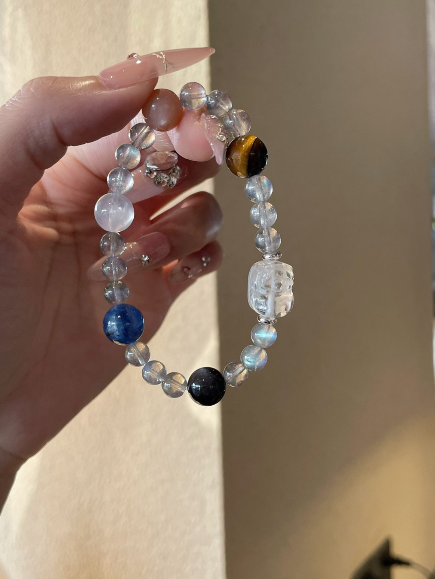 Hand holding the mixed-gem beaded bracelet with a hand-carved clear-quartz centerpiece.