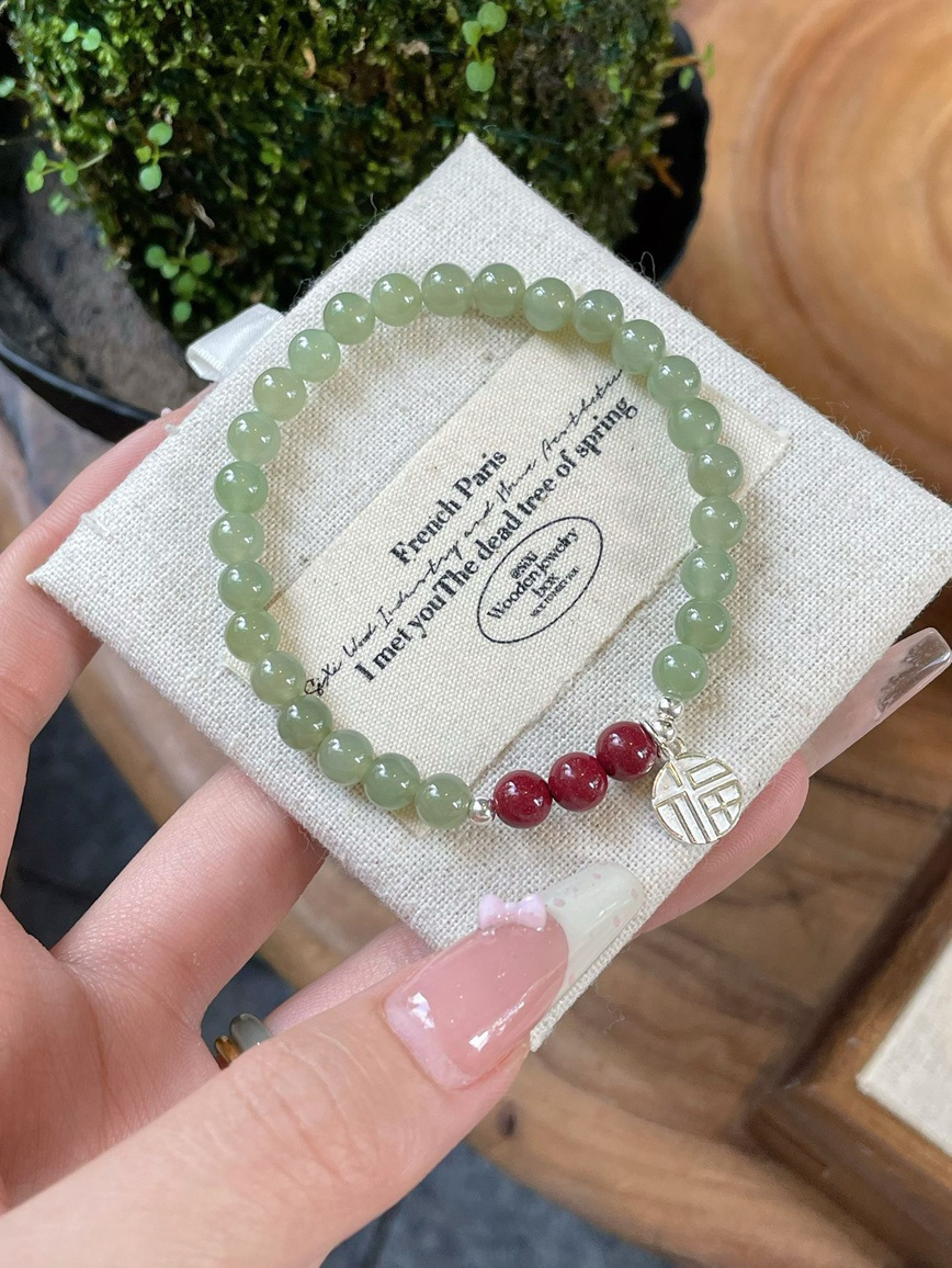 Hetian jade and cinnabar bracelet with silver charm displayed in linen box