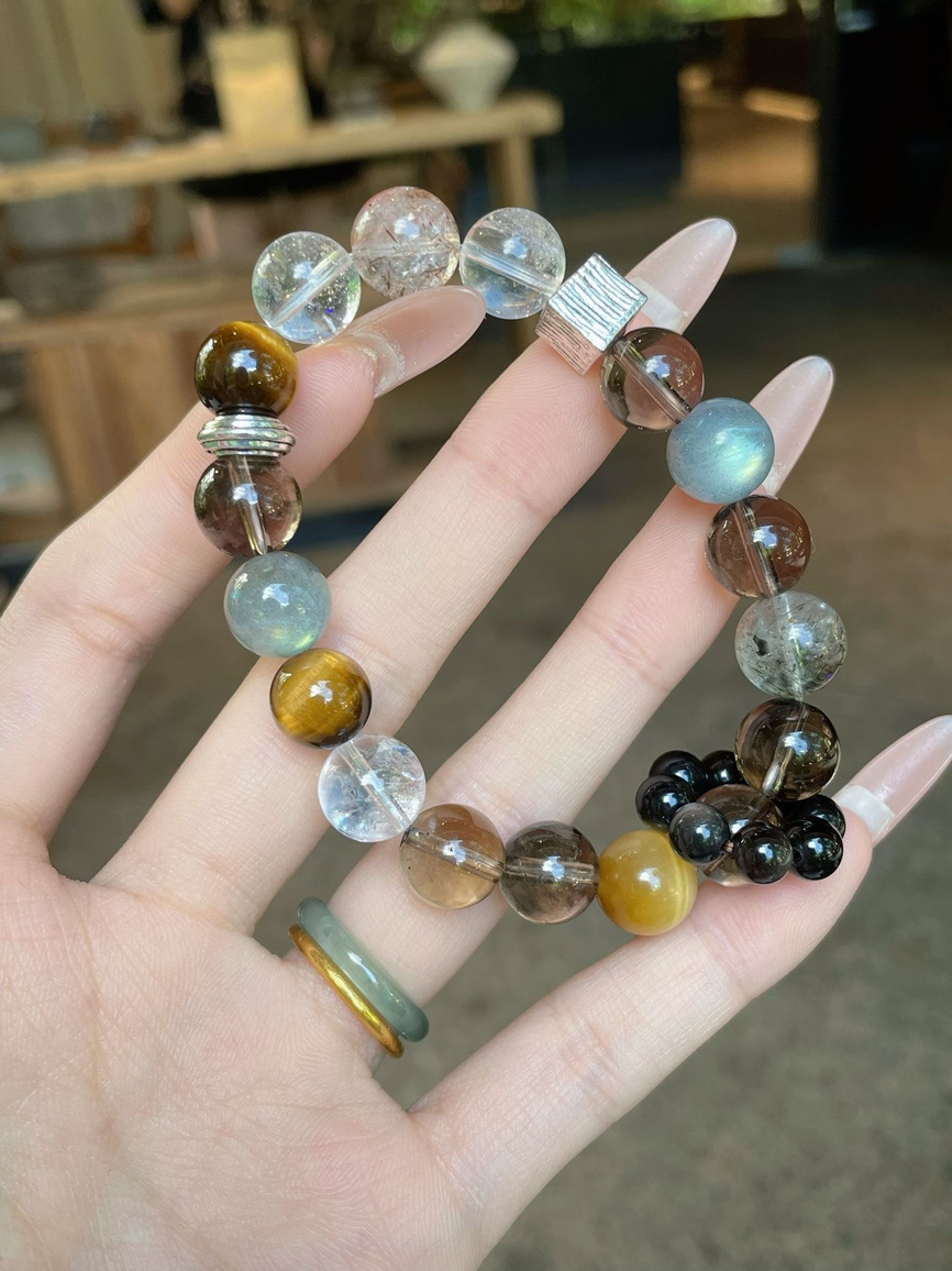 Hand holding natural crystal bracelet featuring smoky quartz, tiger eye, and moonstone.