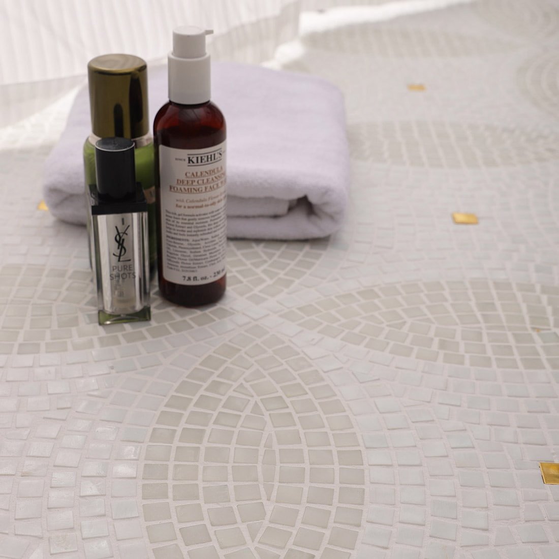 Close-up of white four-leaf clover glass mosaic floor with gold accents and bath products.