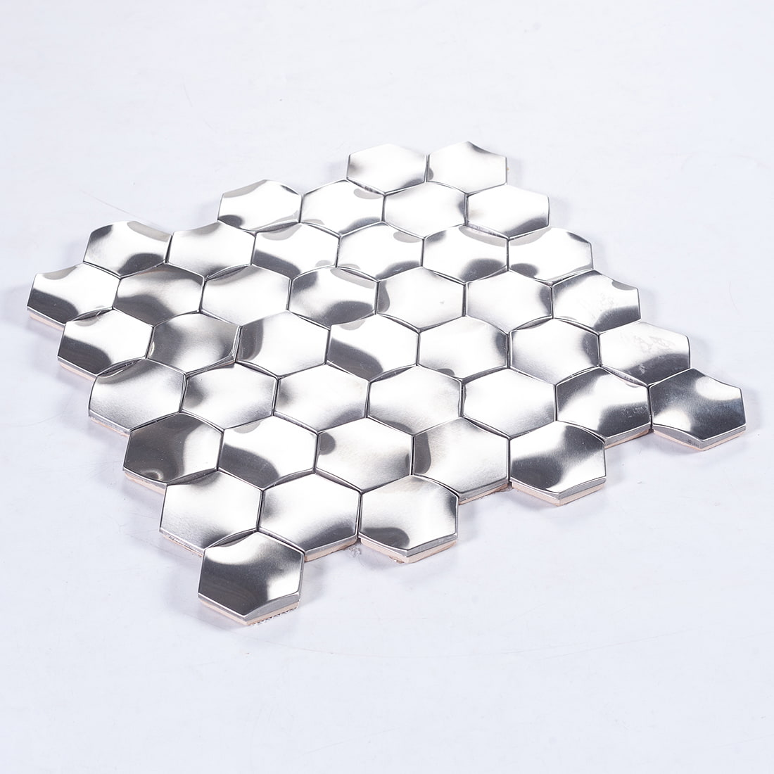 Perspective view of a silver 3D hexagon metal mosaic tile sheet on a white surface.