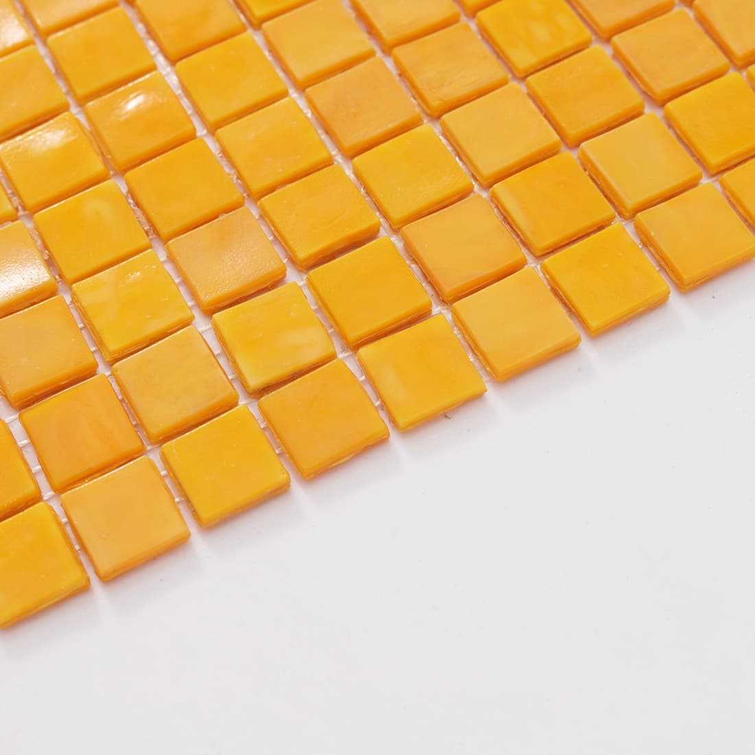 Perspective view of a yellow glass mosaic tile sheet edge against a white surface.