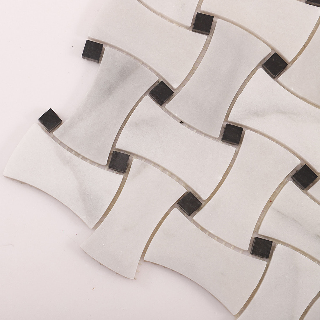 Angled close-up of basketweave marble mosaic with black square dots and grout lines.