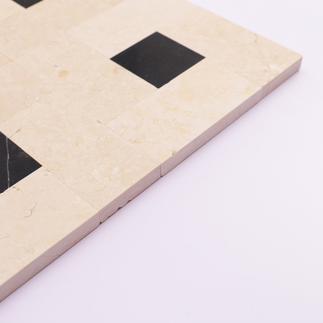 Side edge of beige black marble mosaic tile showing natural stone thickness