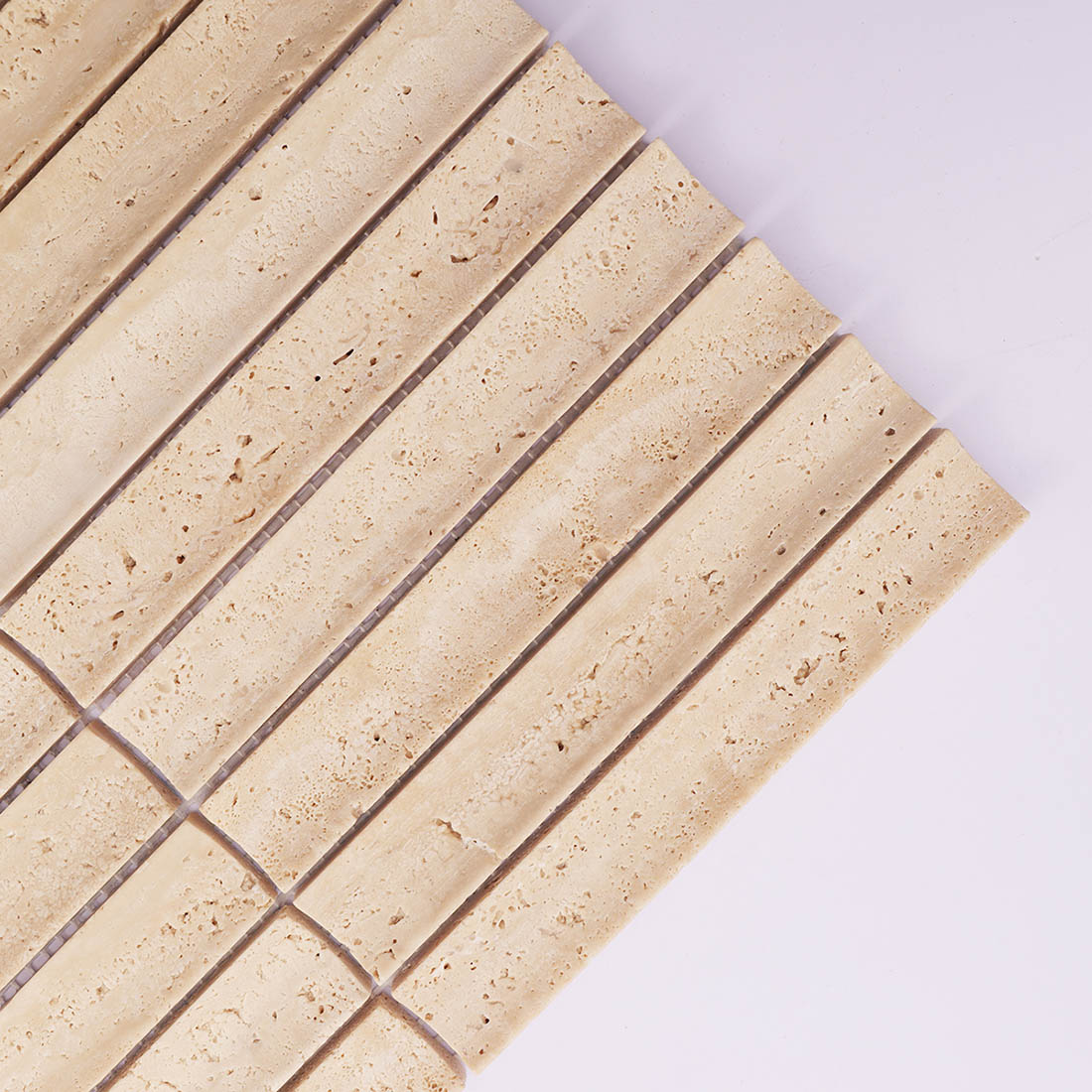 Corner detail of beige grooved travertine mosaic tile with natural porous texture