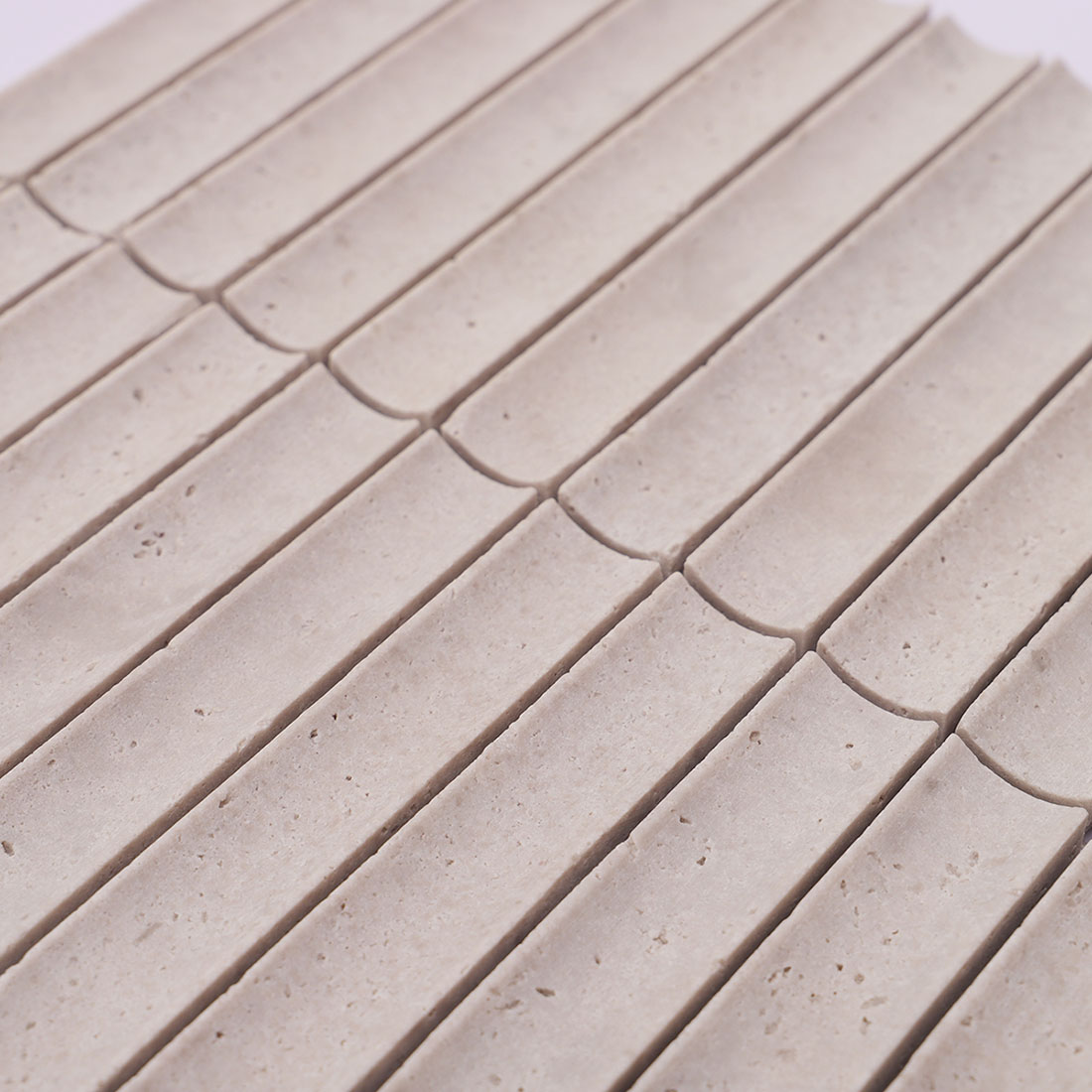 Close-up of light gray grooved travertine mosaic tiles with rounded ends
