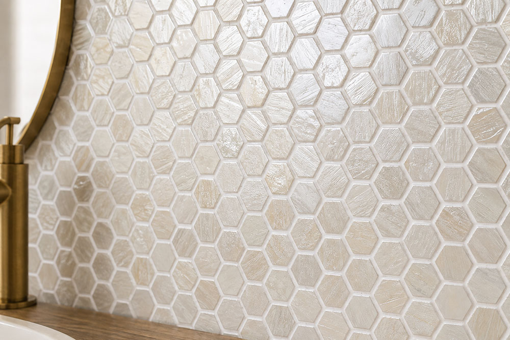 Beige hexagon glass mosaic tile backsplash beside a brass faucet and wood countertop