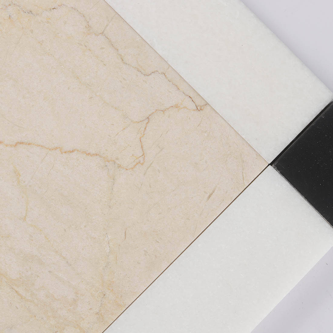 Close-up of beige marble center tile with white border and black corner accent