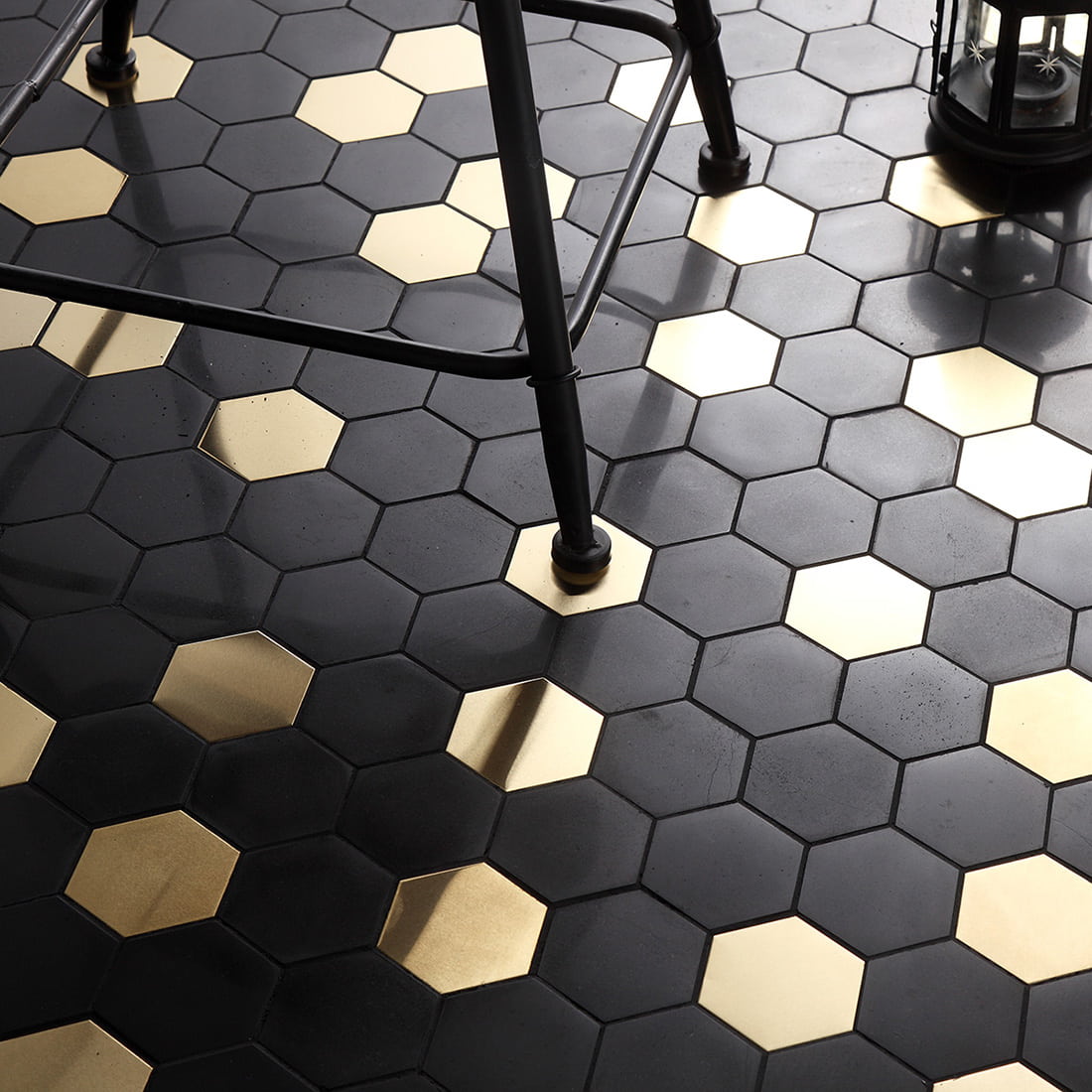 Close-up of installed black and gold hexagonal mosaic floor tiles with a chair leg.