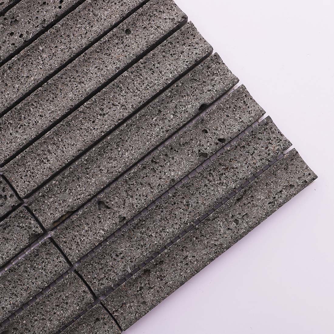 Corner close-up of charcoal gray grooved porous lava stone mosaic tile