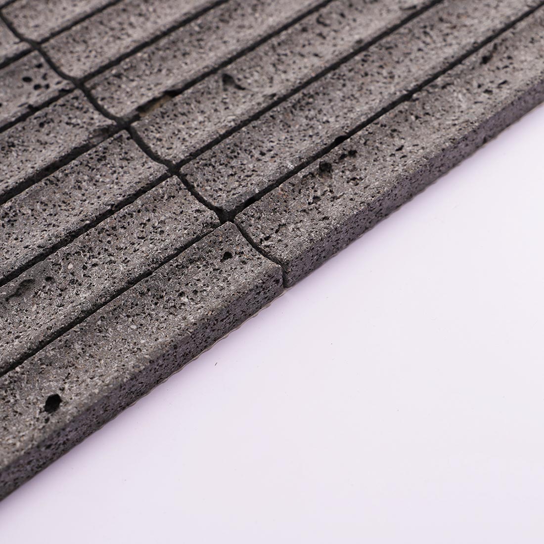 Side edge of charcoal gray grooved lava stone mosaic tile with porous texture
