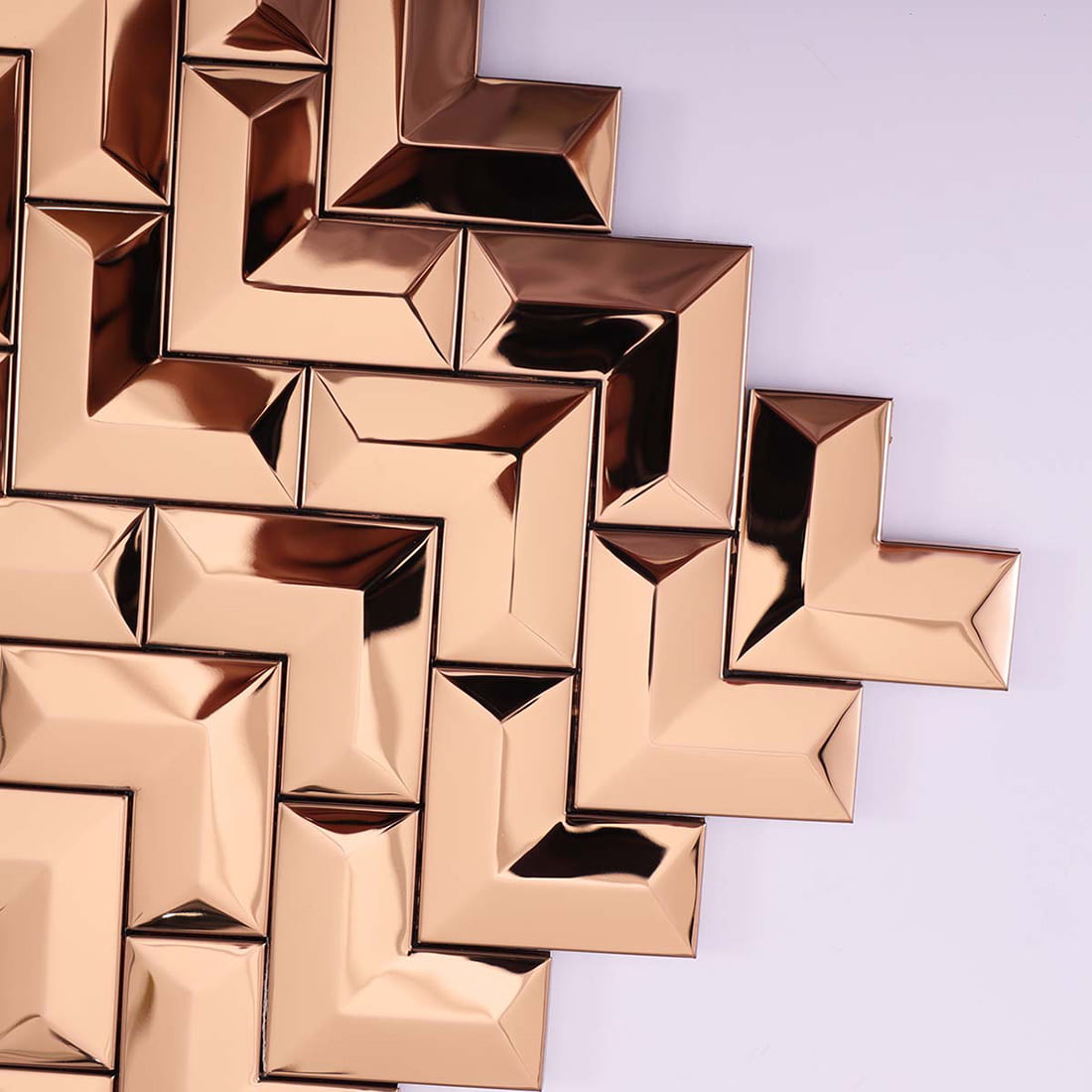 Close-up view of the reflective edges and corner of a rose gold chevron metal tile.