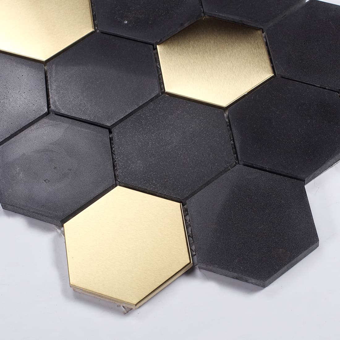Close-up angled shot of black cement and gold metal hexagonal mosaic tiles.