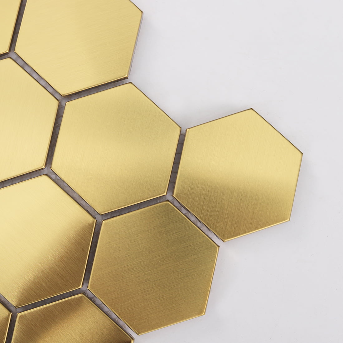 Close-up view of large brushed gold hexagon metal mosaic tiles on a white background