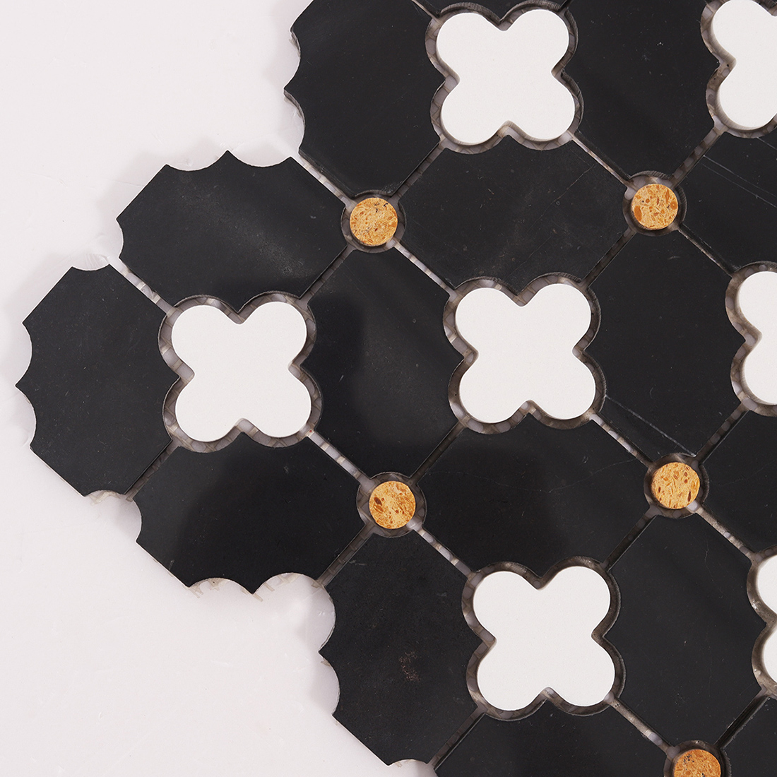 Close up corner of clover mosaic showing cut edge, grout gaps, and gold dots