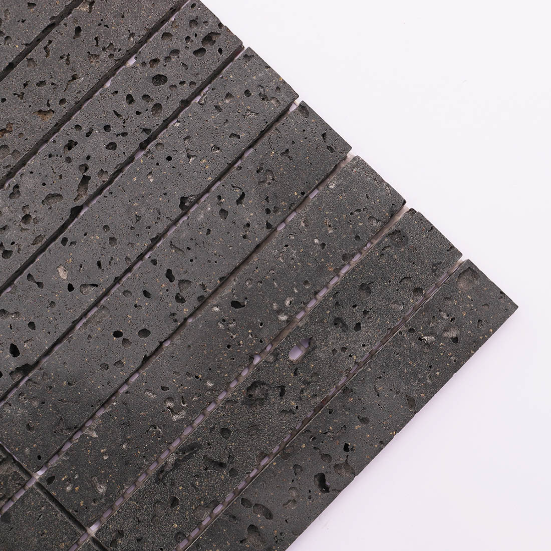 Corner detail of dark gray lava stone stacked mosaic tile with natural pores