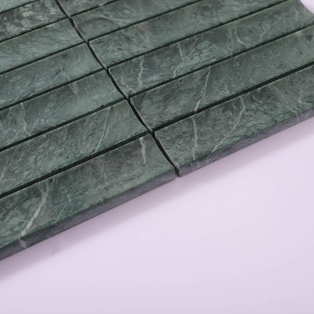 Edge view of dark green marble strip mosaic showing thickness and stone layers