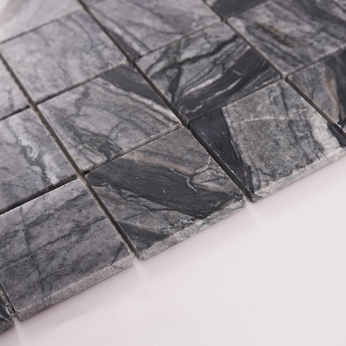 Side angle view showing thickness and edge detail of dark gray marble mosaic tiles
