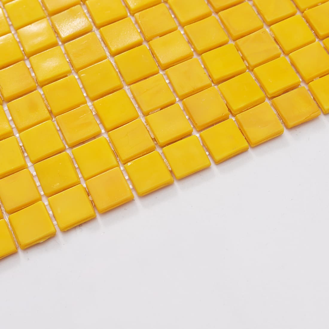 Close-up edge view of bright yellow square glass mosaic tiles showing thickness