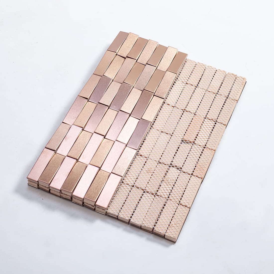Rear view of rose gold stainless steel mosaic tiles showing white fiber mesh backing.
