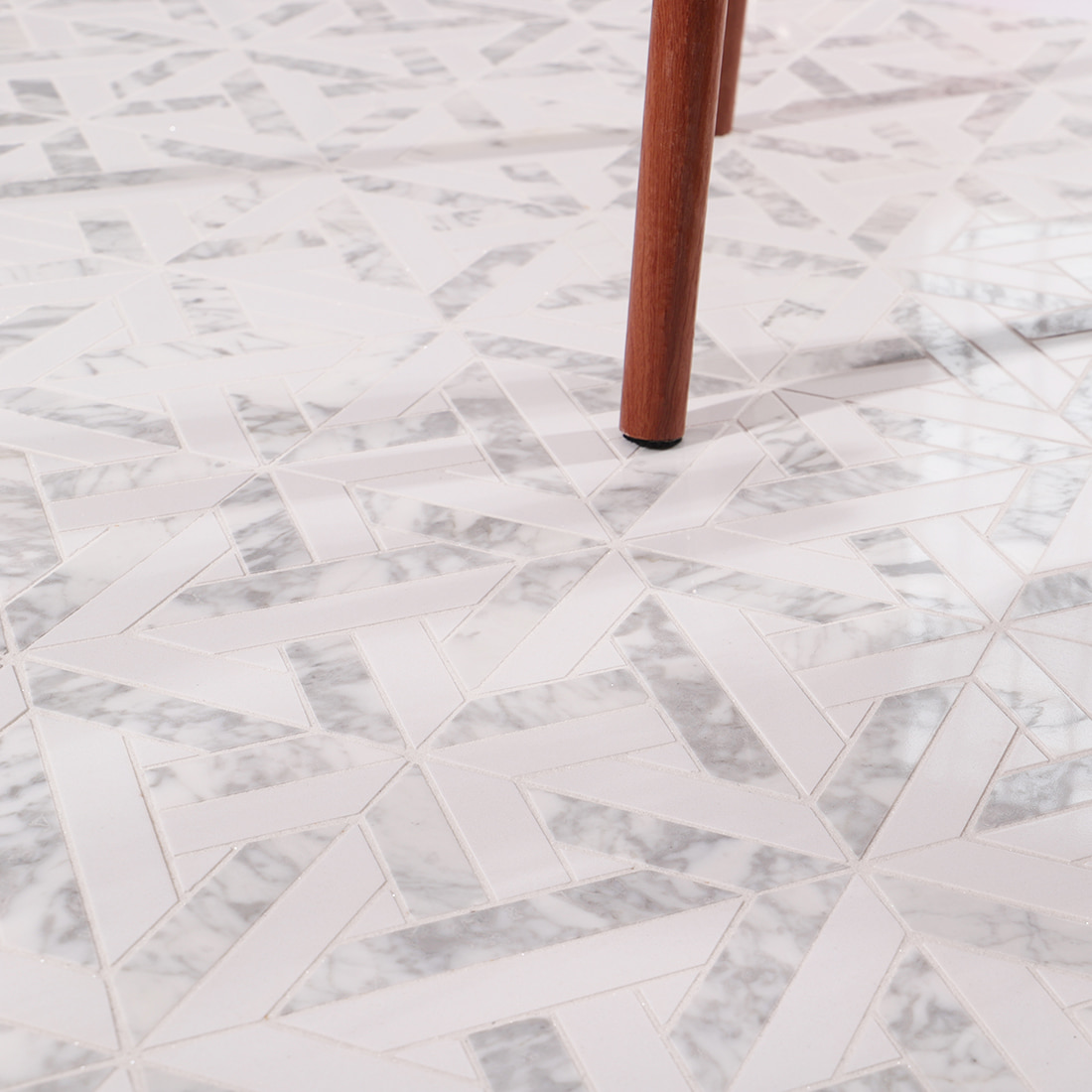 Close up of installed geometric marble mosaic floor with a wooden chair leg