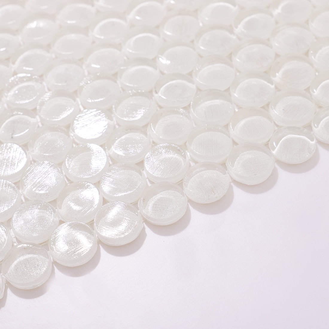 Angled view of glossy white circular glass mosaic tiles with light reflection.