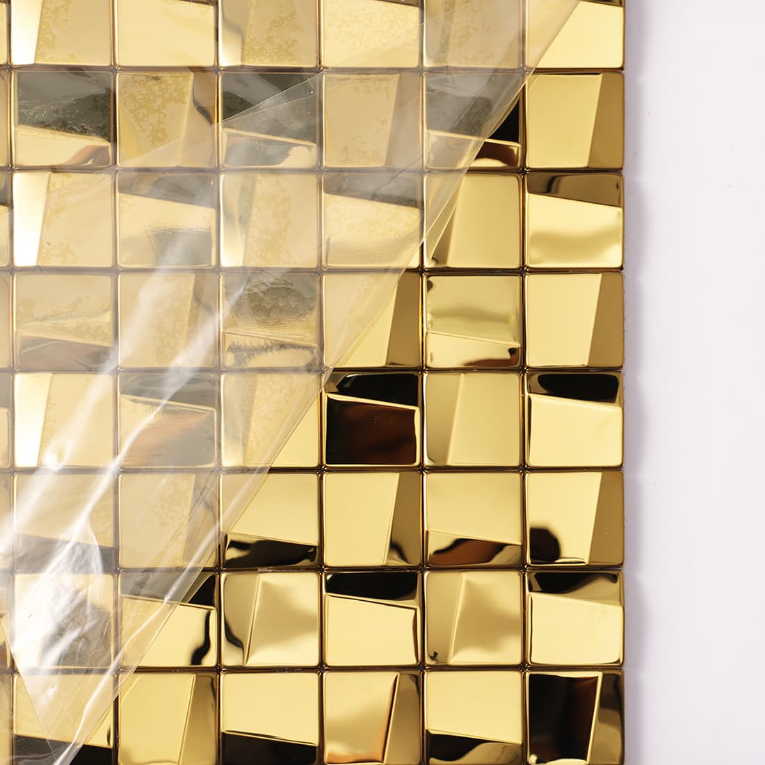 Gold 3D square mosaic tile sheet with protective film being peeled from the surface.