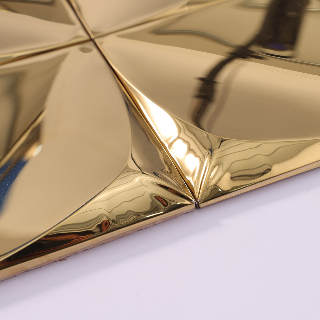 Side detail of gold 3D stainless steel square tiles showing raised facets