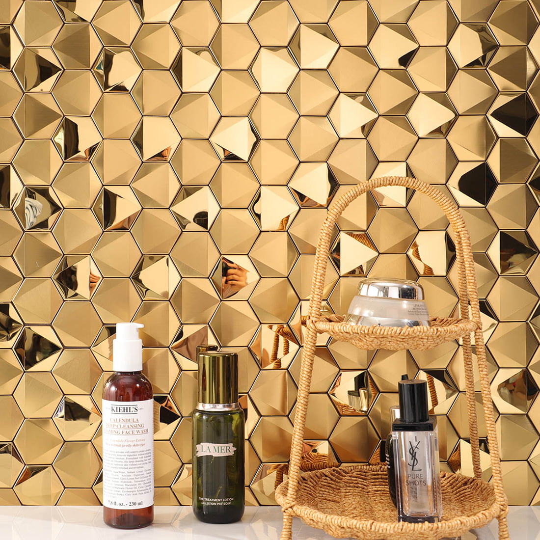 Luxury gold hexagon tile wall behind skincare products and a wicker stand.