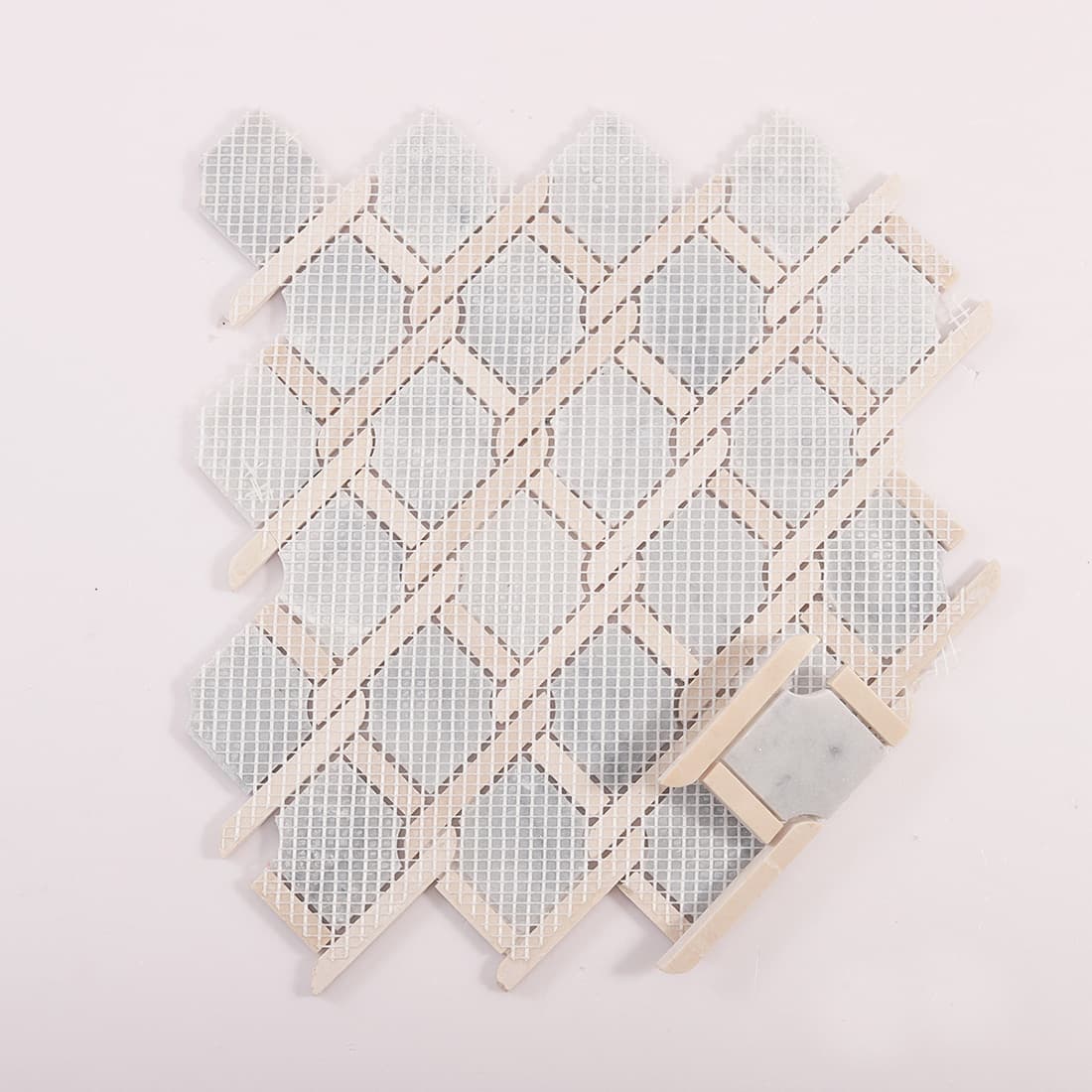 Back view of mosaic tile sheet showing mesh backing and a lifted corner sample